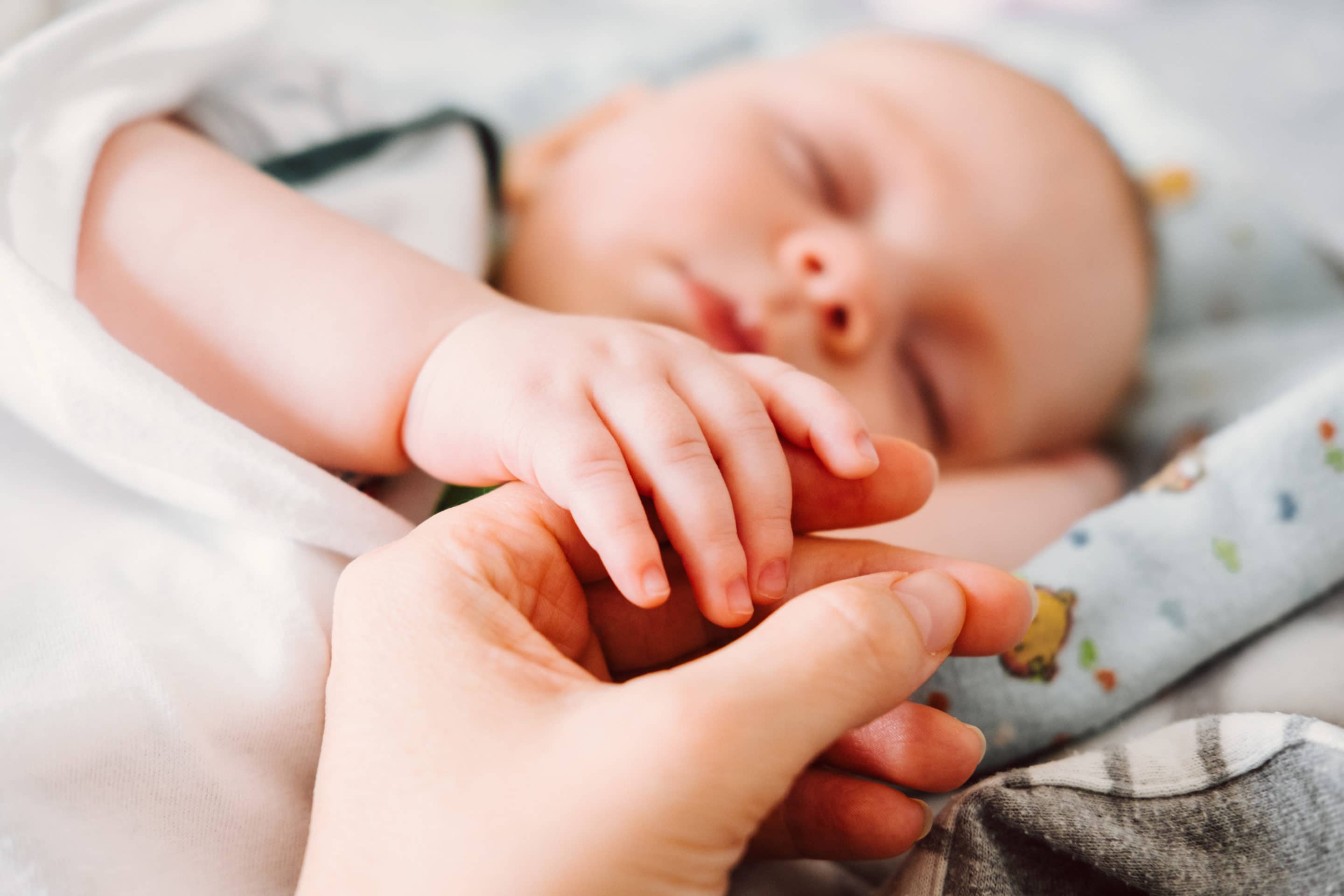 Cute newborn baby holding mother's hand while sleeping. Happy Family concept.